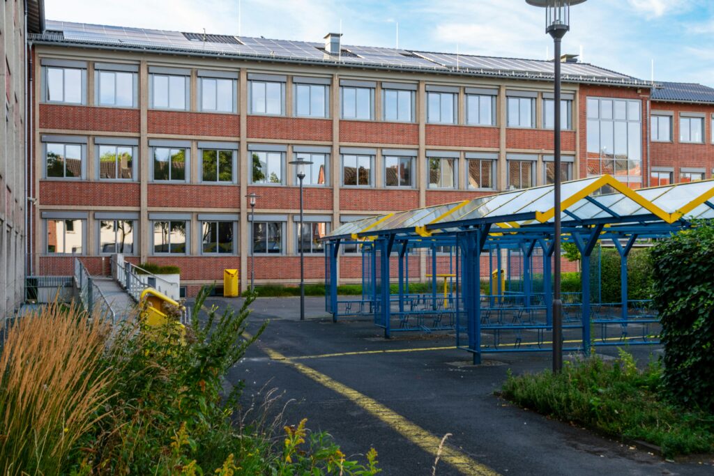School building with solar panels, blue bicycle racks, and greenery. Sunny day.