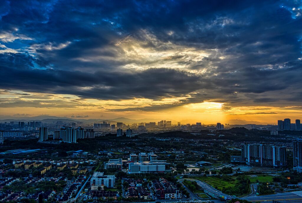 Aerial view of Kuala Lumpur skyline at sunset, showcasing a dramatic sky and urban landscape.